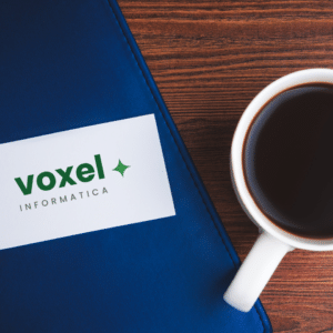 Biglietto da visita Voxel Informatica posato su copertina blu vicino a tazza di caffè su tavolo in legno